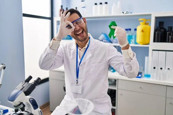 Young Hispanic Man Beard Working Scientist Laboratory Holding Green Ribbon — Stockfoto