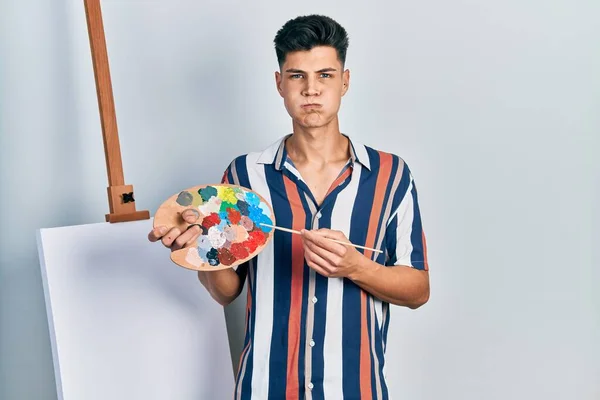 Young Hispanic Man Holding Painter Palette Paintbrush Standing Close Canvas —  Fotos de Stock