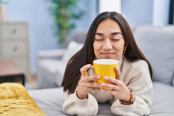 Young Hispanic Woman Drinking Coffee Lying Sofa Home — Stockfoto