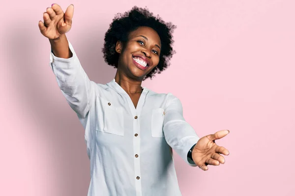 African american woman with afro hair wearing casual white t shirt looking at the camera smiling with open arms for hug. cheerful expression embracing happiness.