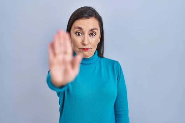 Middle age hispanic woman standing over isolated background doing stop sing with palm of the hand. warning expression with negative and serious gesture on the face.