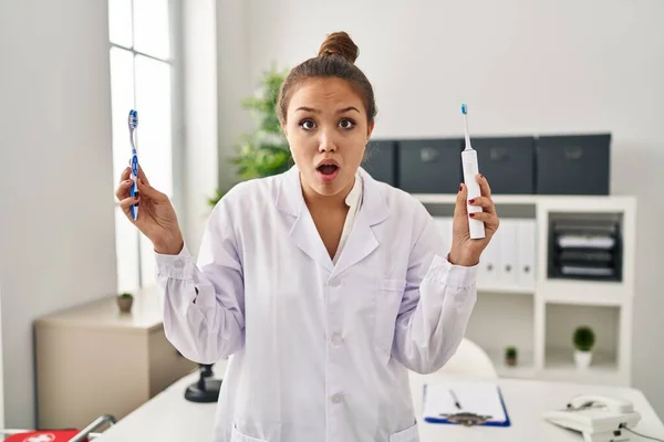Young Hispanic Dentist Woman Holding Ordinary Toothbrush Electric Toothbrush Afraid — Stock Photo, Image