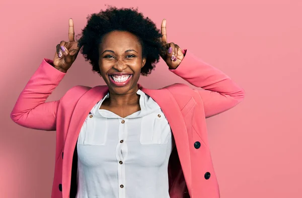African american woman with afro hair wearing business jacket posing funny and crazy with fingers on head as bunny ears, smiling cheerful