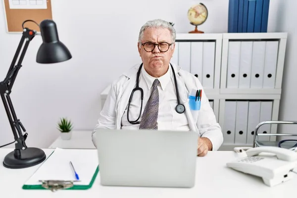 Senior Kaukasische Man Draagt Doktersuniform Stethoscoop Bij Kliniek Puffend Wangen — Stockfoto