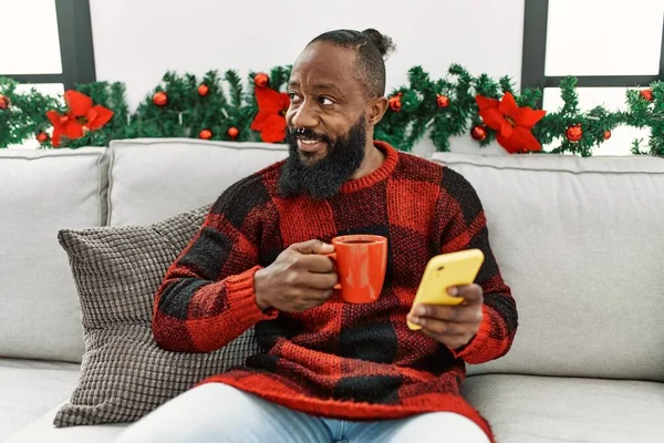 Young African American Man Drinking Coffee Using Smartphone Sitting Christmas — Zdjęcie stockowe