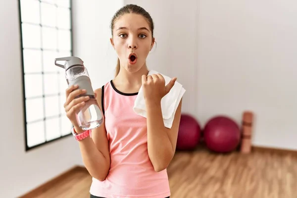 Young Brunette Teenager Wearing Sportswear Holding Water Bottle Surprised Pointing — Stockfoto