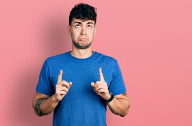 Gündelik tişört giyen genç İspanyol adam üzgün ve üzgün görünüyor, parmaklarıyla yönü gösteriyor, mutsuz ve depresif.. 