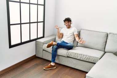 Genç İspanyol adam evde müzik dinlerken kendinden emin gülümsüyor.