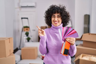 Yeni ev duvarının rengini seçen kıvırcık saçlı genç esmer kadın gülümsüyor. 