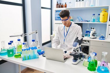 Laboratuvarda dizüstü bilgisayar kullanan Latin kökenli genç adam.