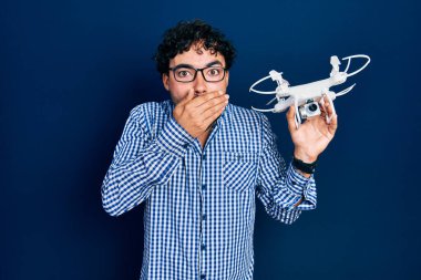Genç İspanyol asıllı bir adam drone 'u elinde tutarak ağzını eliyle kapatıyor, şok geçiriyor ve hata yapmaktan korkuyor. şaşırmış ifade 