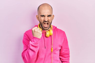 Spor kıyafetleri giyen, kulaklık takan kızgın ve kızgın genç kel bir adam öfkeyle bağırırken yumruğunu kaldırıyor. öfke ve agresif konsept. 