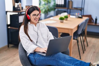 Young hispanic woman business worker using laptop and headphones working at office