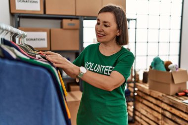 Orta yaşlı İspanyol kadın bağış standında bağışlanan kıyafetlere bakıyor.