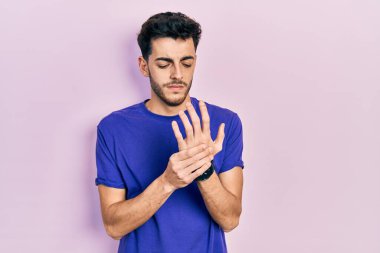 Ellerinde ve parmaklarında ağrı, eklem iltihabı olan gündelik tişört giyen İspanyol genç bir adam. 