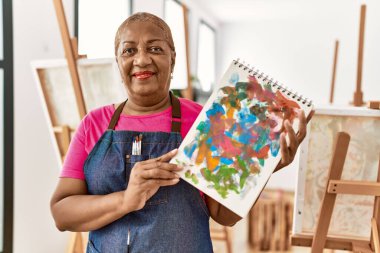 Kıdemli Afro-Amerikan kadın gülümsüyor sanat stüdyosunda kendine güvenen çizim defteri tutuyor.