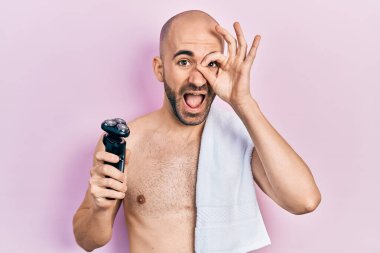 Tıraş bıçağı tutan kel genç adam gülümsüyor mutlu oluyor. El ve göz işaretleriyle parmaklarından bakıyor. 