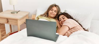 Genç çift yatak odasında dizüstü bilgisayar kullanarak film izliyor.