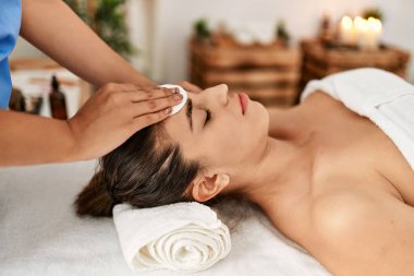 İki kadın terapist ve hasta güzellik merkezinde yüz bakımı yaptırıyor.