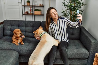Genç İspanyol kadın akıllı telefonun başında köpeklerle kanepede otururken selfie çekiyor.