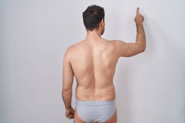 İspanyol asıllı genç adam iç çamaşırsız, ters poz vermiş, parmaklarıyla öne bakıyor. 