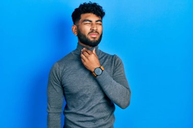 Balıkçı yaka kazak giyen sakallı bir Arap, ağrılı boynuna dokunuyor, grip, mantar ve enfeksiyon yüzünden boğazı ağrıyor. 