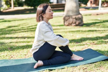 Orta yaşlı bir kadın parkta gerinirken kendine güvenerek gülümsüyor.