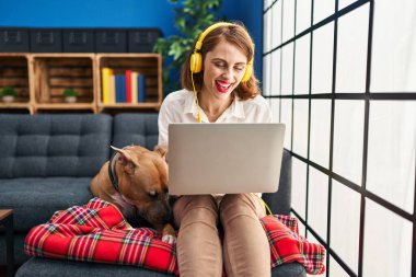 Young beautiful woman using laptop sitting on the sofa looking positive and happy standing and smiling with a confident smile showing teeth 