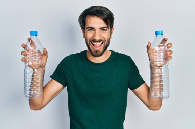 Genç İspanyol adam elinde plastik şişelerle gülüyor ve kahkahalarla gülüyor.. 