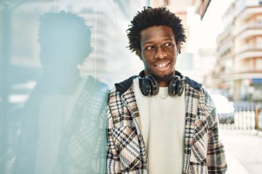 Afro saçlı, kulaklık takan yakışıklı, açık havada mutlu gülümseyen bir zenci.