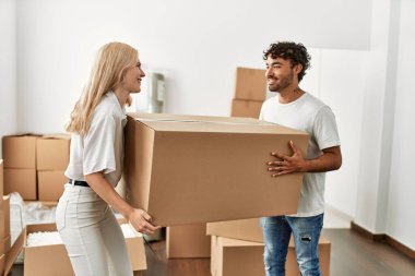 Genç ve güzel bir çift mutlu bir şekilde gülümsüyor. Yeni evlerinde büyük bir karton kutu tutuyorlar..