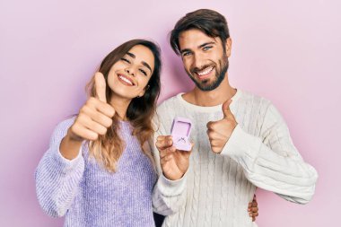 Evlenme teklifi için nişan yüzüğü tutan güzel bir çift. Mutlu ve olumlu gülümseyen, mükemmel ve onay işareti yapan bir çift. 