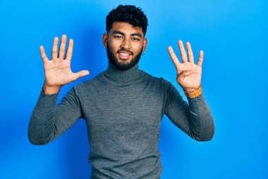 Balıkçı yaka kazak giyen sakallı bir Arap dokuz numarayı gösterip işaret ederken kendinden emin ve mutlu gülümsüyor.. 