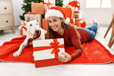 Genç Kafkas kadın boks hediyesini açıyor. Evde yılbaşı ağacının yanında köpekle yatıyor.