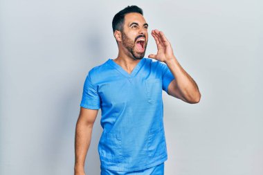 Sakallı yakışıklı, mavi erkek hemşire üniforması giyen, el ve ağızla bağırıp çağıran bir İspanyol. iletişim konsepti. 