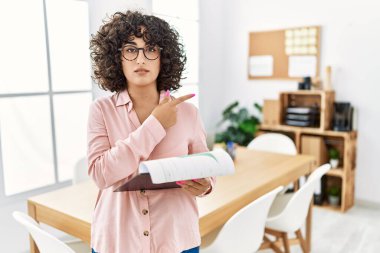 Ofiste iş elbisesi giyen genç ortadoğulu bir kadın el ile işaret ederek reklamını yapıyor, ciddi ve sakin bir yüz ifadesi var. 