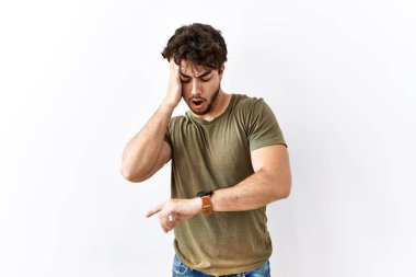 Hispanic man standing over isolated white background looking at the watch time worried, afraid of getting late 