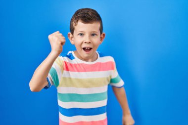 Kafkasyalı genç, mavi arka planda öfkeli ve kızgın duruyor öfkeyle bağırırken yumruğunu kaldırıyor. öfke ve agresif konsept. 