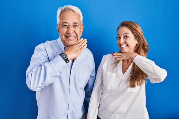 Middle Age Hispanic Couple Standing Blue Background Cutting Throat Hand — Stockfoto