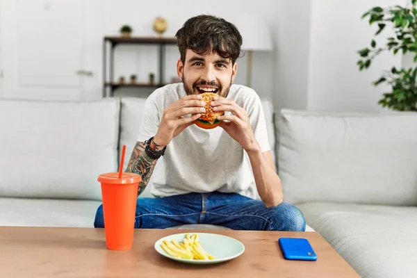 Latin Kökenli Genç Adam Klasik Burger Yiyor Evdeki Kanepede Soda — Stok fotoğraf