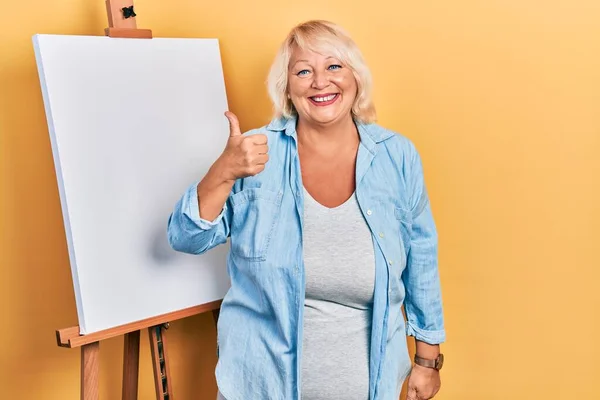 Middle Age Blonde Woman Standing Painter Easel Stand Smiling Happy — Stockfoto