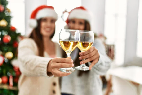 两个女人举着香槟酒敬酒 互相拥抱 站在家里的圣诞树旁 — 图库照片