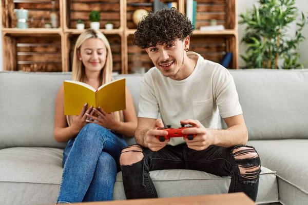 Young Couple Smiling Happy Playing Video Game Reading Book Home — ストック写真