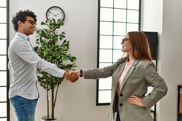 Two business workers smiling happy shaking hands at the office