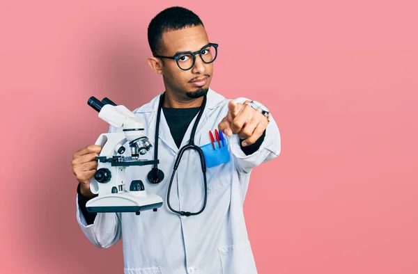 Joven Hombre Afroamericano Vistiendo Uniforme Científico Sosteniendo Microscopio Señalando Con — Foto de Stock