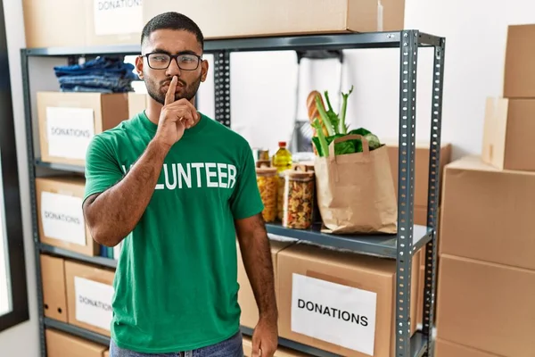 Young indian man volunteer holding donations box asking to be quiet with finger on lips. silence and secret concept. 
