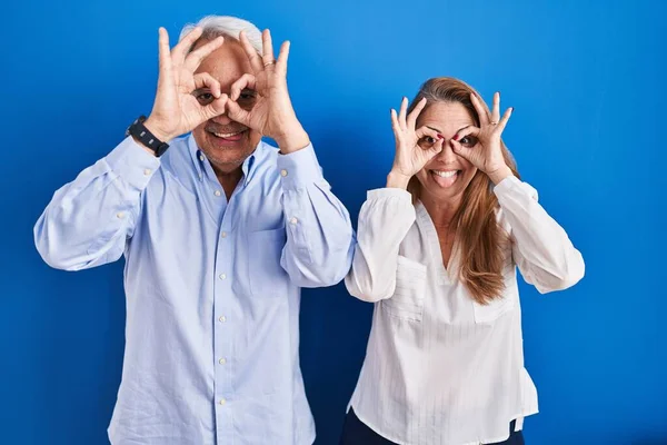 Middle Age Hispanic Couple Standing Blue Background Doing Gesture Binoculars — Φωτογραφία Αρχείου