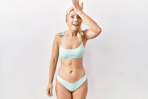 Young caucasian woman wearing bikini over isolated background surprised with hand on head for mistake, remember error. forgot, bad memory concept.