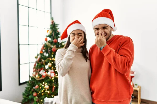 Young Hispanic Couple Standing Christmas Tree Smelling Something Stinky Disgusting — Stock Fotó