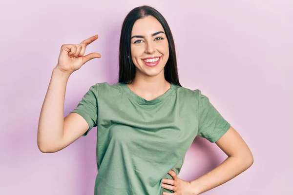 Beautiful woman with blue eyes wearing casual t shirt smiling and confident gesturing with hand doing small size sign with fingers looking and the camera. measure concept.